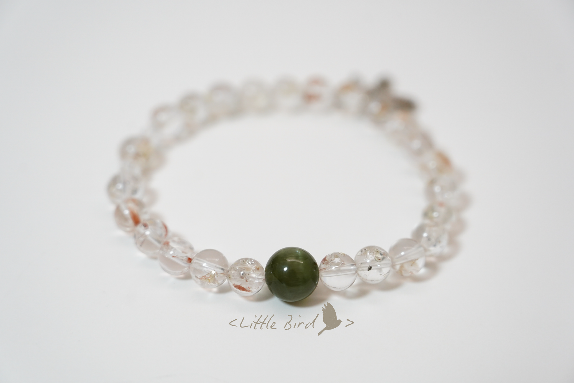 Crystal bracelet with clear beads and a green stone on a white background, branded 'Little Bird'.