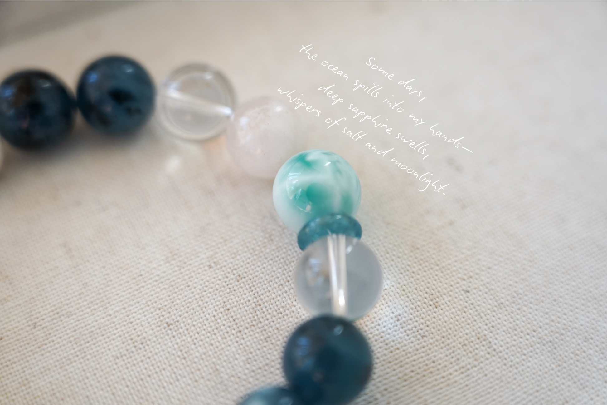 Close-up of a beaded crystal bracelet with blue, green, and clear beads on a textured surface.