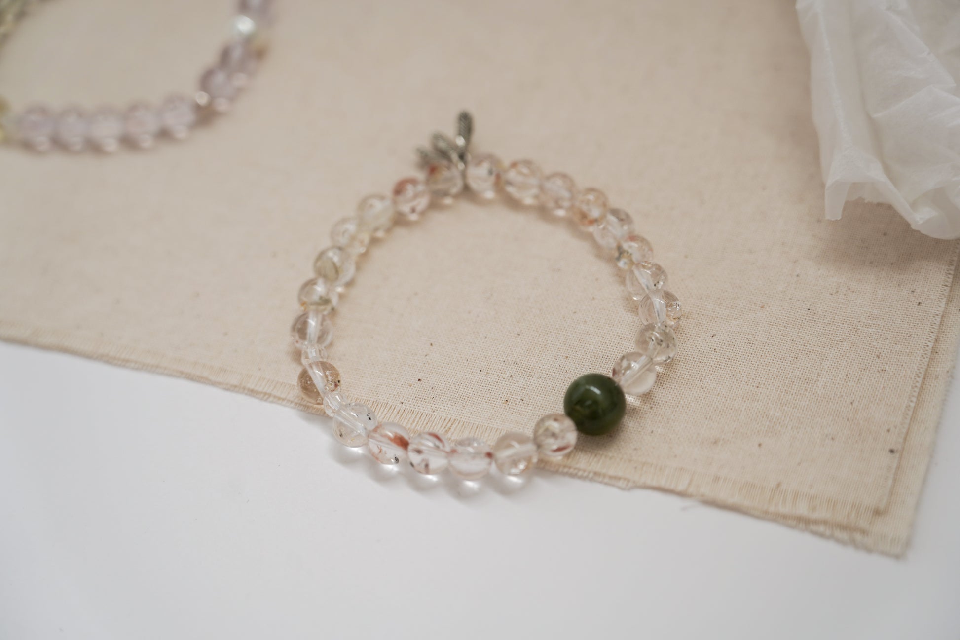 Crystal bracelet with a green bead on a beige fabric background