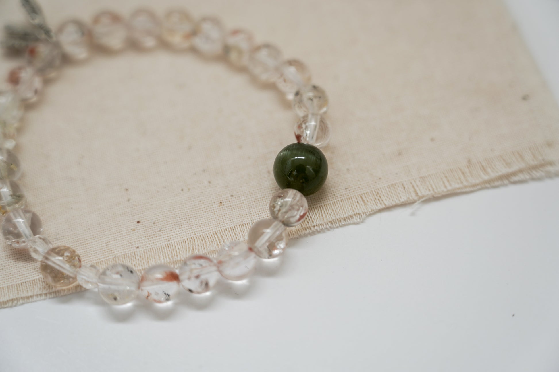 Crystal bracelet with clear beads and a green bead on a beige fabric background