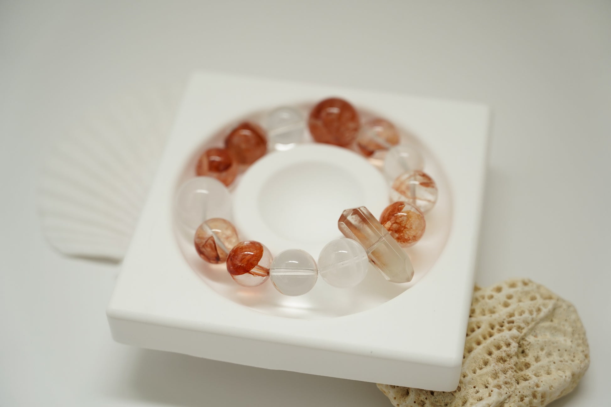 Amber Dawn Crystal Bracelet with red and clear beads on a white dish with a natural stone background