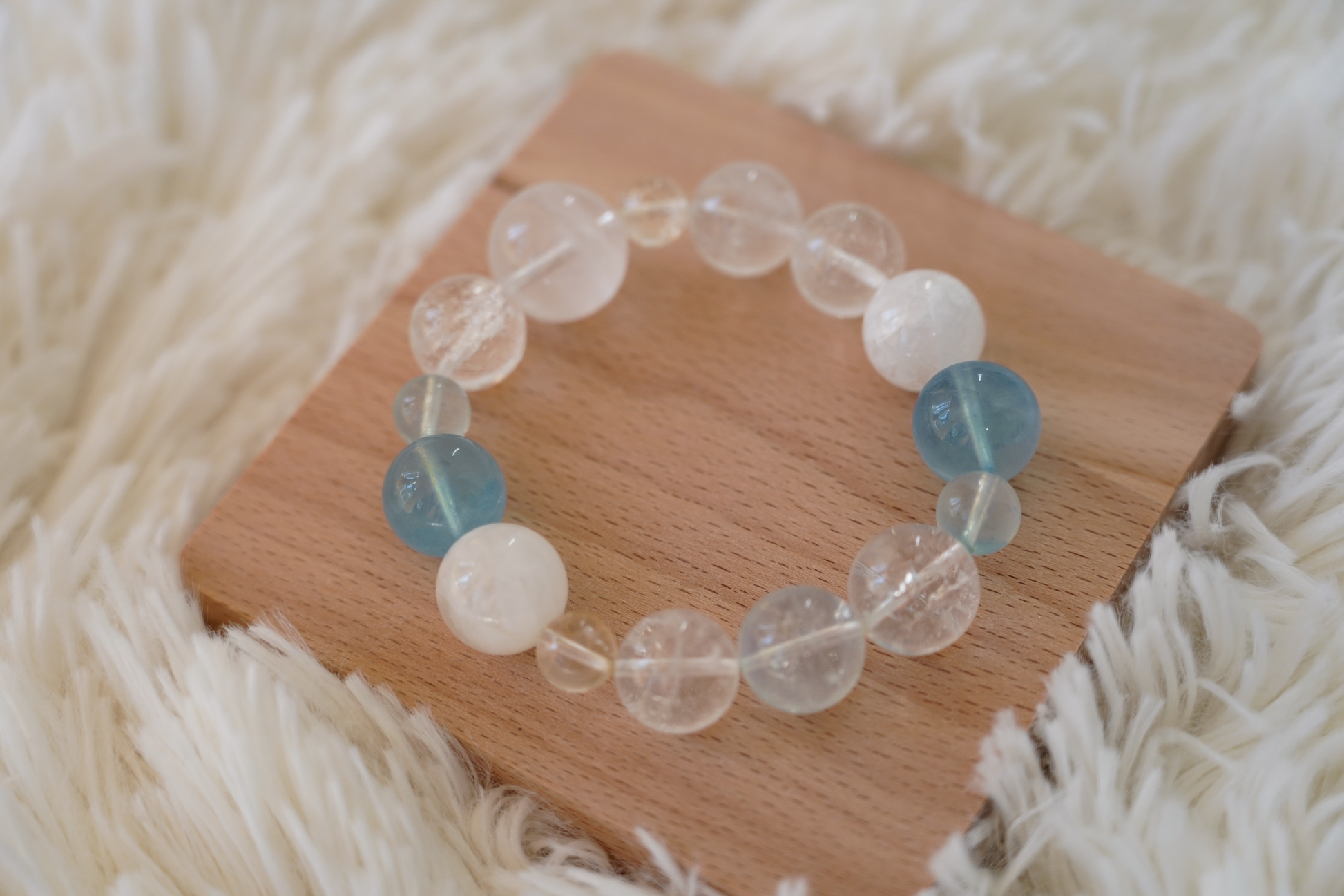 Beaded bracelet with clear, white, and blue beads on a wooden board with a soft white background