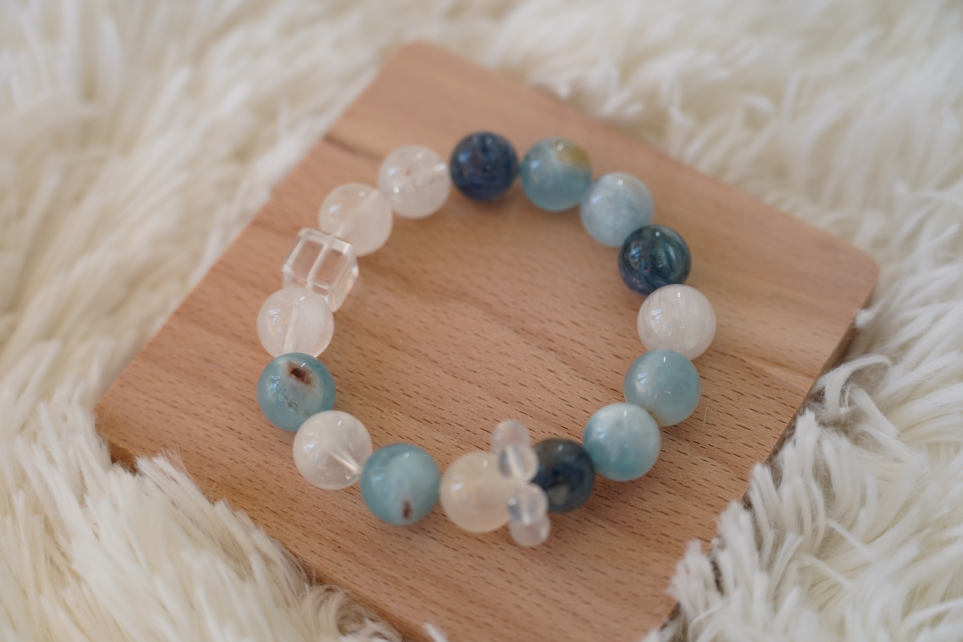 Beaded crystal bracelet with blue, white, and clear beads on a wooden block with a soft white background