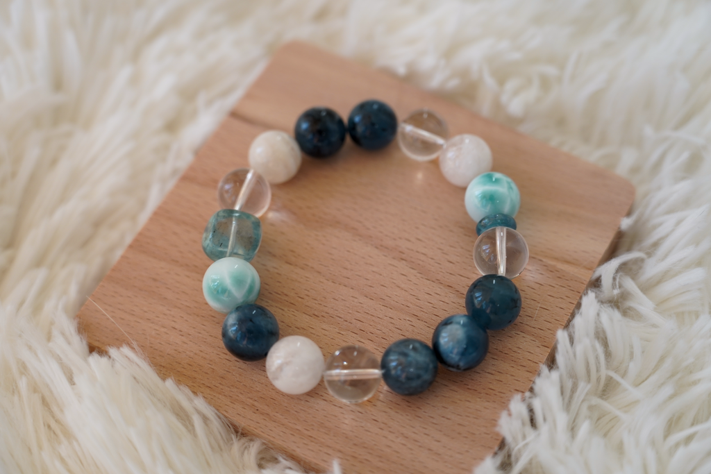 Beaded crystal bracelet with blue, green, and clear beads on a wooden board with a soft white background