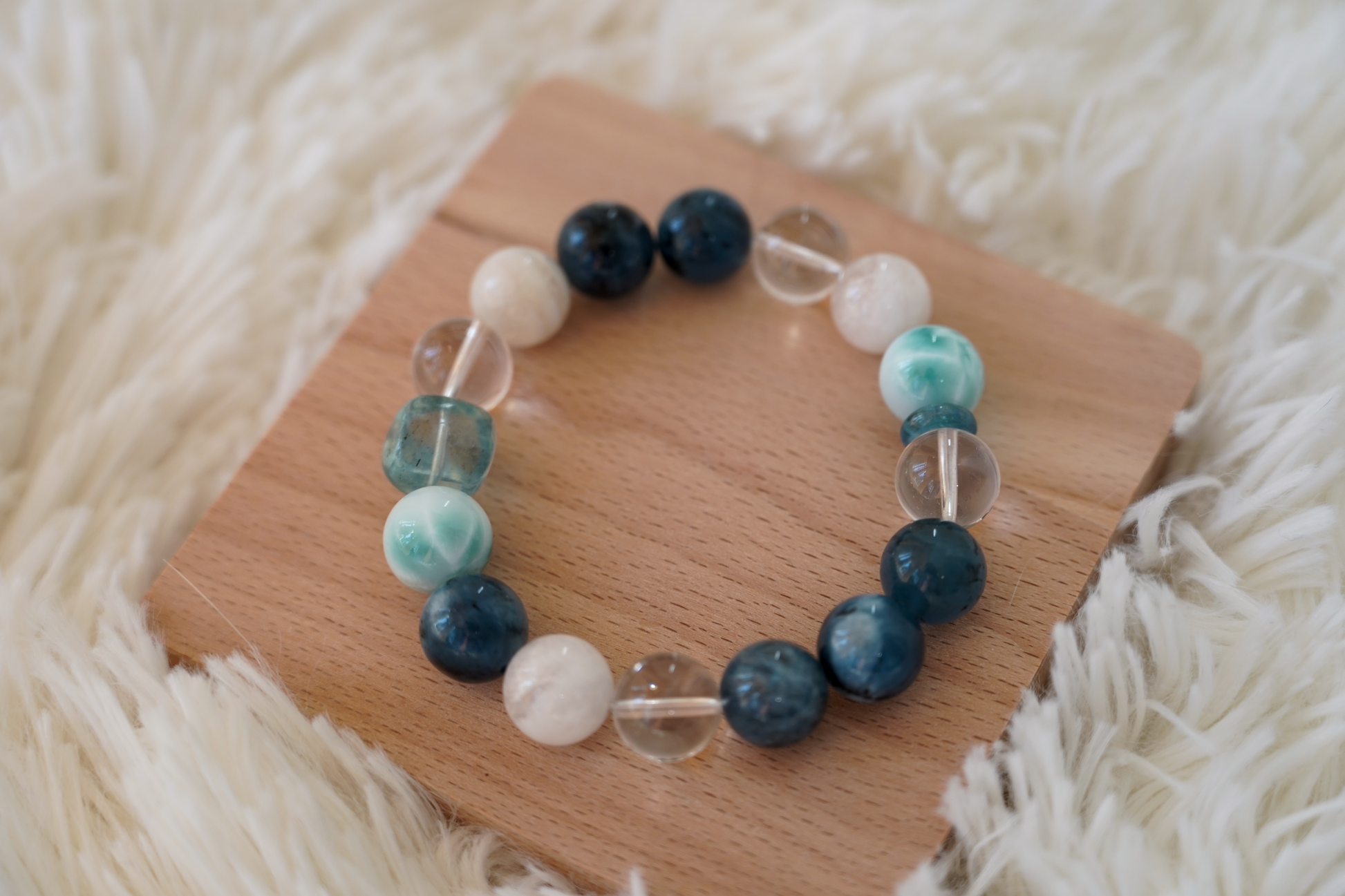 Beaded crystal bracelet with blue, green, and clear beads on a wooden board with a soft white background